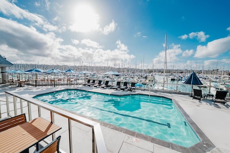 A pool area with lounge chairs and umbrellas, overlooking a marina with numerous boats.