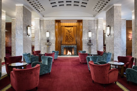 A lobby with a fireplace, red and blue chairs, marble walls, and wall sconces.