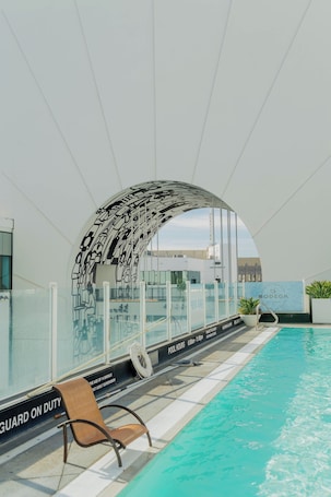 A modern indoor pool with clear poolside seating and a distinctive arched ceiling design.