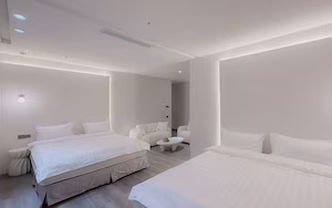 A modern hotel room with a large bed, a smaller bed, two chairs, and a small table.