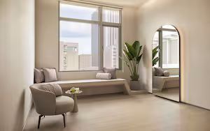 A modern room with a large window, a built-in bench, a potted plant, and a round mirror.