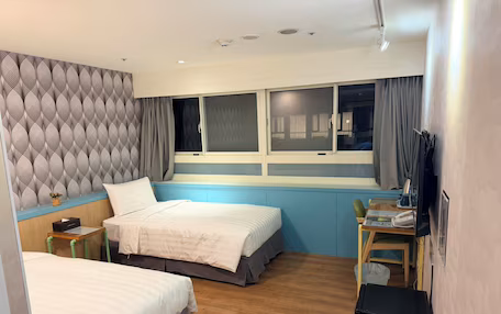 A hotel room with two beds, a desk with a chair, a TV, and a window with curtains.