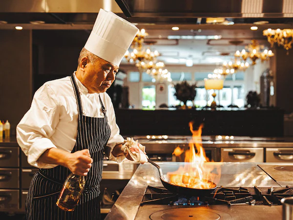 A chef cooking with a pan on a stove in a kitchen setting.