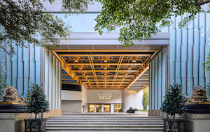 A modern building entrance with a covered walkway, steps leading up to the entrance, and decorative lion statues.