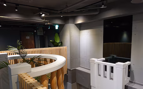 A modern interior with a curved white reception desk, a wooden slatted partition, and a staircase leading to an upper level.