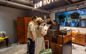 A hotel reception area with a wooden desk, a computer, and a large window with plants.