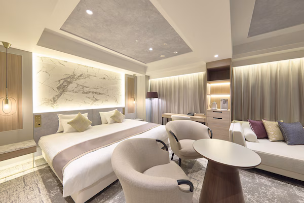 A modern hotel room with a large bed, a sofa, a desk, and a chair.