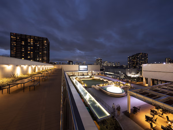 A rooftop terrace with seating, a pool, and city views at night.