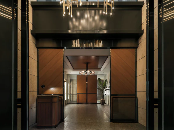 A modern lobby with a central chandelier, wooden paneling, and a reception desk.