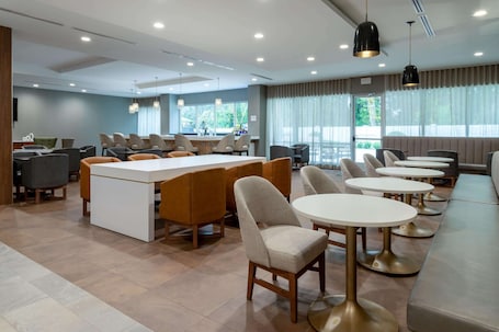 A modern hotel lobby with a central bar area, seating arrangements, and large windows providing natural light.