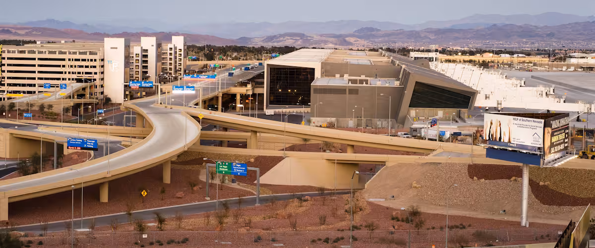 A highway interchange with multiple overpasses, a parking garage, and a large building with a distinctive roof.